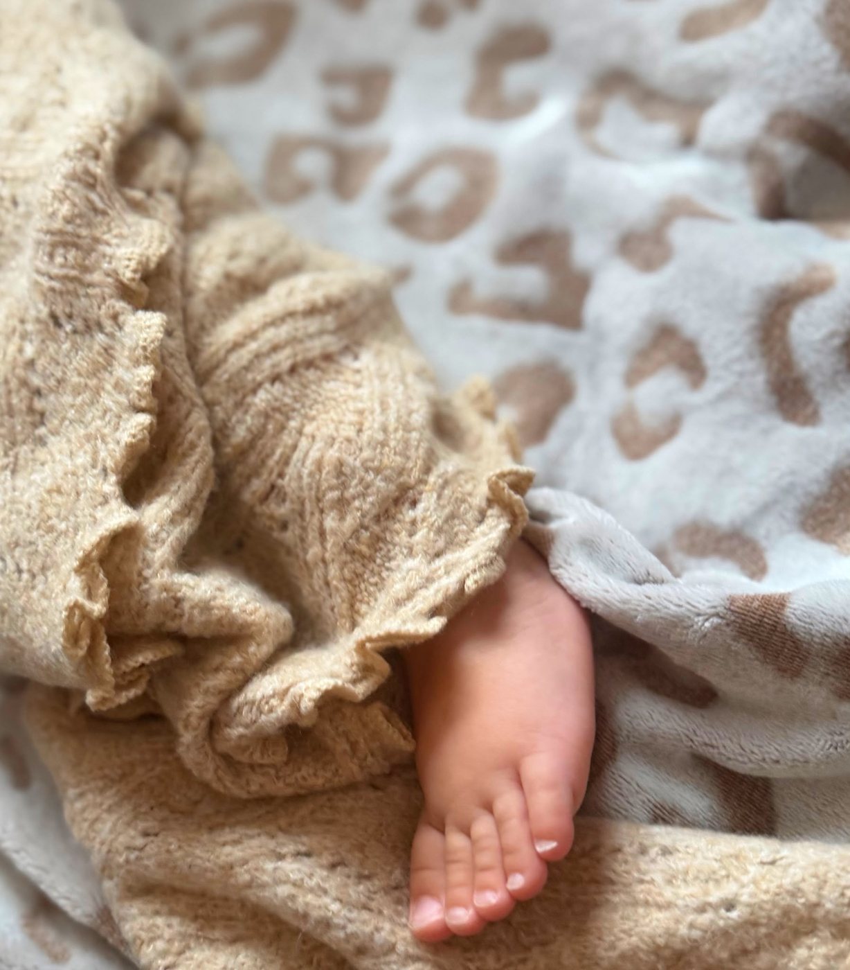 Babyfuß schaut unter einer Strickdecke hervor